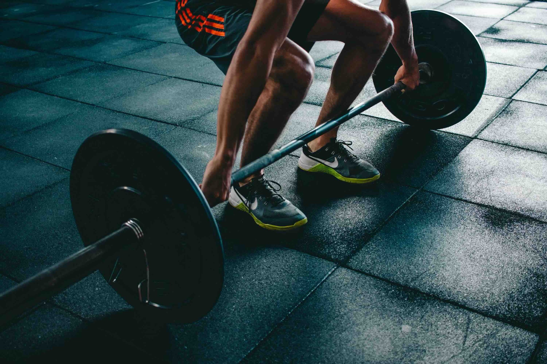 Lifter setting up to deadlift a loaded barbell on a dark gym floor