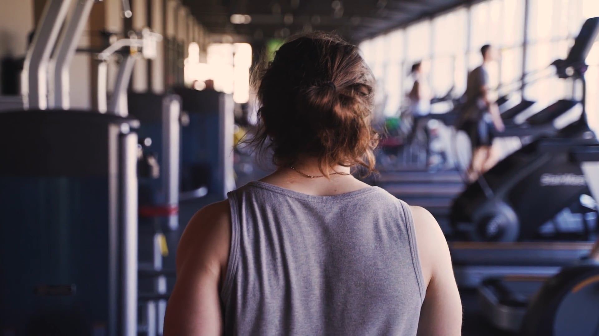 Lifter walking down a bright gym floor between rows of cardio machines